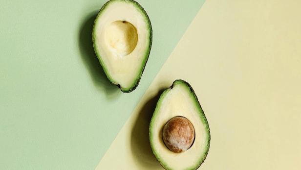 Zwei halbe Avocados liegen auf einem zweifarbigen Hintergrund.