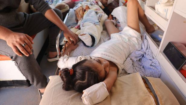 Ein kleines, palästinensisches Mädchen liegt auf einem Krankenhausbett. Ihre beiden Arme sind verbunden. In einem stecken Vorrichtungen, um einen offenen Bruch zu behandeln, auf dem anderen scheint die Hand amputiert worden zu sein.