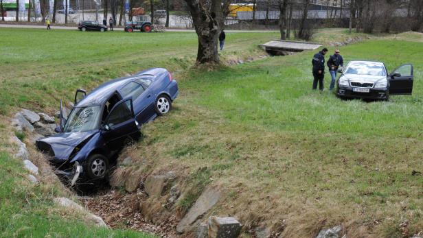 Ein blaues Auto ist in einen Graben gefahren, während Polizisten ein anderes Auto untersuchen.