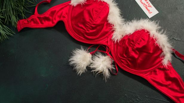 Ein roter BH mit weißem Fellbesatz liegt neben einer Weihnachtskarte.