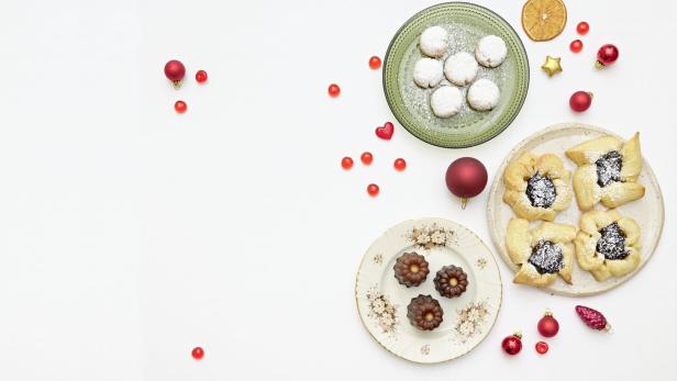 Verschiedene Weihnachtsplätzchen und rote Zuckerstreusel sind auf Tellern angerichtet.