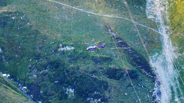 Ein Rettungshubschrauber landet in einem bergigen Gelände in der Nähe einer Gruppe von Personen.