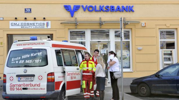 Ein Rettungswagen des Samariterbundes steht vor einer Bank, während Sanitäter mit Passanten sprechen.