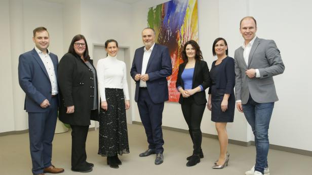 Eine Gruppe von sechs Personen posiert vor einem farbenfrohen Gemälde.