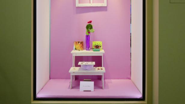 Ein Schaukasten mit rosa Wänden, einem Fensterrahmen und einem kleinen Tisch mit Dekorationen.