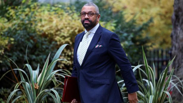 James Cleverly mit Brille und Anzug, eine rote Mappe in der Hand.