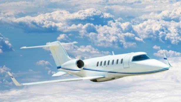 Ein weißes Privatflugzeug fliegt über den Wolken.