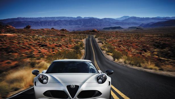 Ein silberner Alfa Romeo 4C fährt auf einer Landstraße in Richtung einer Bergkette.