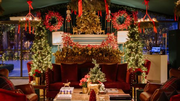Ein festlich dekorierter Wohnraum mit Weihnachtsbäumen, Kränzen und roten Akzenten.