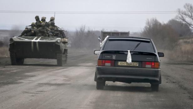 Ein Schützenpanzer mit Soldaten fährt hinter einem Lada auf einer unbefestigten Straße.