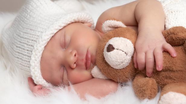 Ein schlafendes Baby mit Mütze umarmt einen Teddybären.