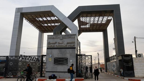 A man stands in a gate while people gather at the Rafah border