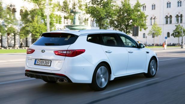 Ein weißer Kia Optima Sportswagon fährt auf einer Straße in der Stadt.
