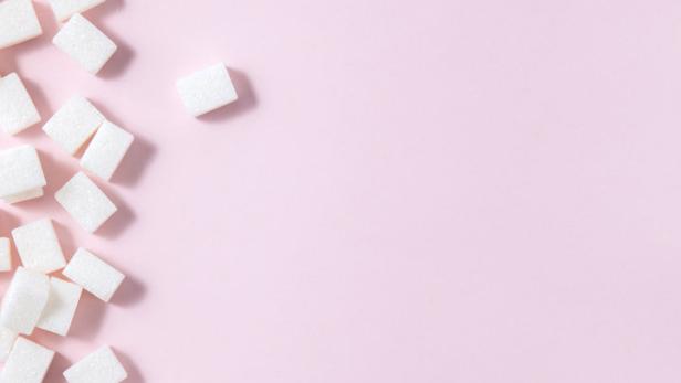 Zuckerwürfel liegen auf einem rosa Hintergrund.