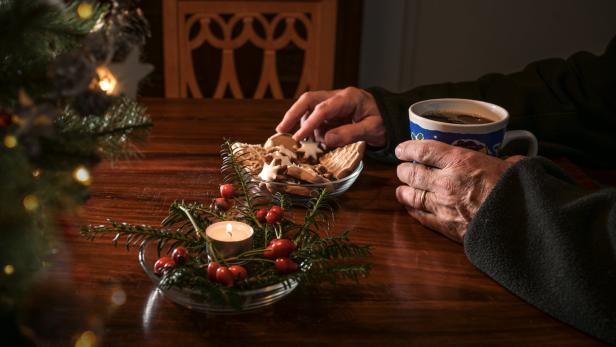 Eine Person nimmt einen Keks von einem Teller und hält eine Tasse Kaffee in der Hand.