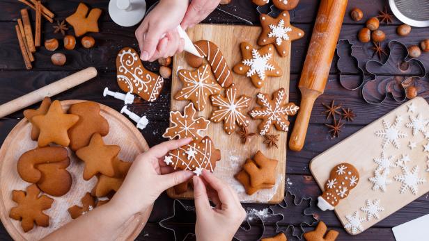 Hände verzieren Lebkuchen mit Zuckerguss auf einem Holztisch.