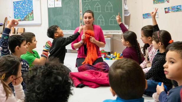 Eine Lehrerin unterrichtet die um sie herum sitzenden Kinder auf dem Boden eines Klassenzimmers