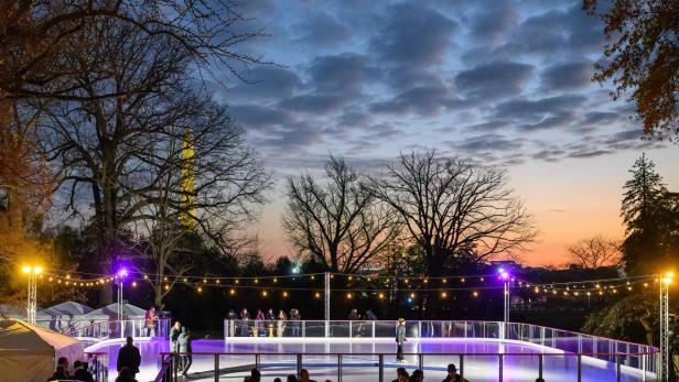 Eine beleuchtete Eisbahn im Freien mit Menschen unter einem bewölkten Himmel bei Dämmerung.