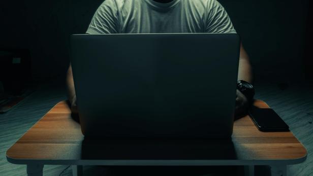 A man in a white shirt sits on a laptop in a dark room. with light shining down. internet concept addiction.topview.