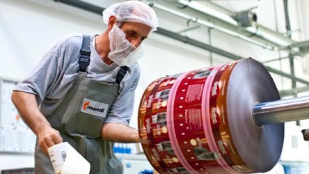 Ein Arbeiter mit Haarnetz und Mundschutz an einer Maschine zur Verpackungsherstellung.