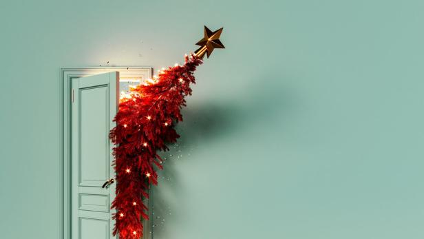 Ein rot geschmückter Weihnachtsbaum scheint aus einer offenen Tür in einem mintgrünen Raum zu wachsen.