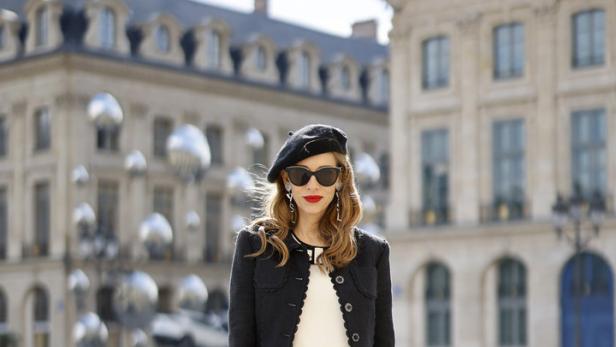 Eine Frau mit Baskenmütze und Sonnenbrille posiert mit einer Handtasche von Yves Saint Laurent in Paris.