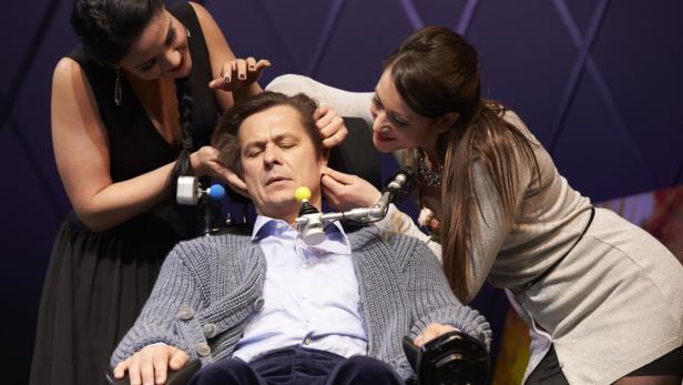 Zwei Frauen kümmern sich um einen Mann im Rollstuhl.