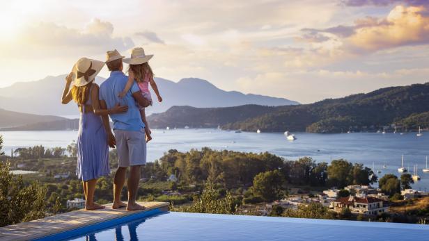 Eine Familie mit Kind genießt die Aussicht von einem Hotelpool auf das Meer.