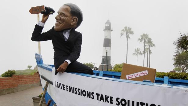 Eine Obama-Puppe sitzt in einem Boot und blickt mit einem Fernglas in Richtung Paris.