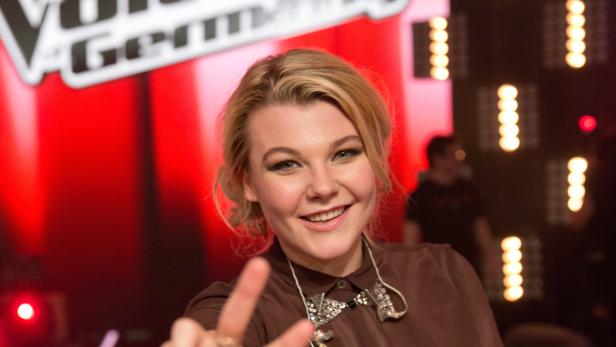 Eine junge Frau lächelt vor dem Hintergrund der „The Voice Germany“-Bühne.