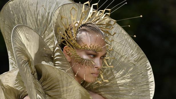 Ein Model präsentiert ein extravagantes goldenes Kleid und einen Kopfschmuck.