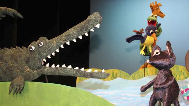 Ein Krokodil mit aufgerissenem Maul und weitere Tierpuppen auf einer Bühne.