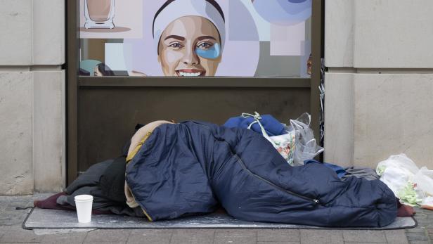 Eine Person liegt in einem Schlafsack vor einem Geschäft mit Kosmetikwerbung.