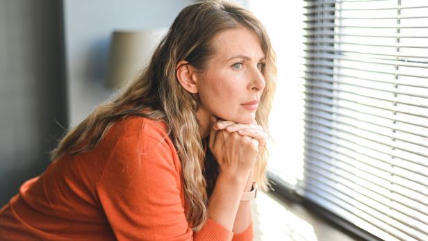 Frau schaut nachdenklich aus dem Fenster