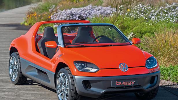Ein orangefarbener VW Buggy steht vor einer blühenden Hecke.