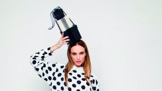 Eine Frau in gepunkteter Kleidung balanciert Geschenkboxen auf dem Kopf.