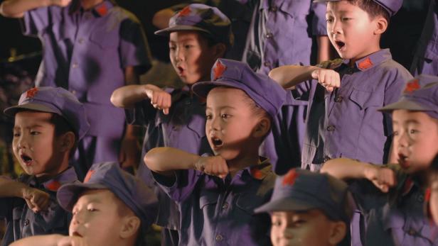 Eine Gruppe Kinder in Uniformen mit roten Sternen singt.