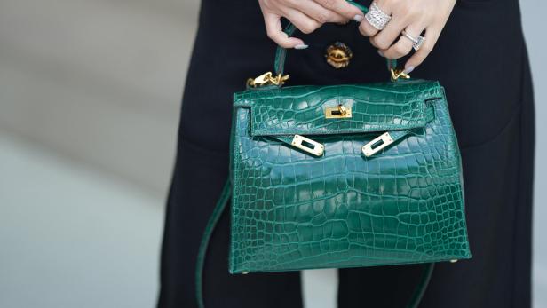 Eine Frau hält eine grüne Krokodillederhandtasche mit goldenen Akzenten.