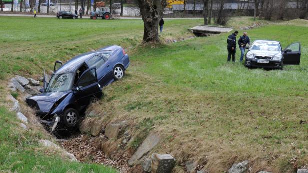 Ein blaues Auto ist in einen Graben gefahren, während Polizisten ein anderes Auto untersuchen.