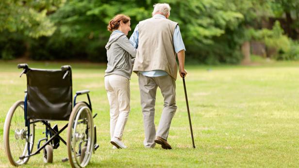 Altenpflegerin hilft einem alten Mann mit Gehstock beim Spaziergang