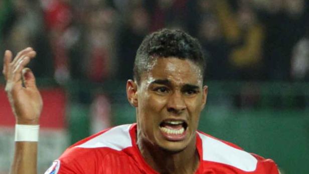 Ein Fußballspieler in rotem Trikot gestikuliert auf dem Spielfeld.