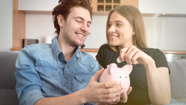 Ein Paar füttert gemeinsam ein rosa Sparschwein mit Münzen.