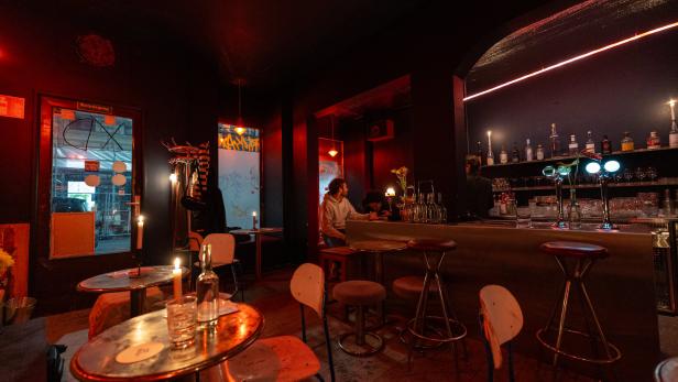 Innenansicht einer Bar mit gedämpftem, rotem Licht und Gästen.