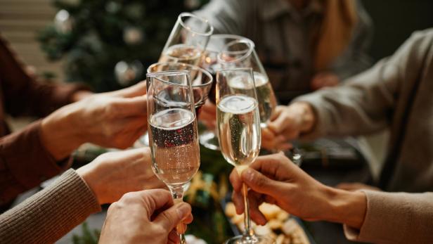 Mehrere Personen stoßen mit Sektgläsern bei einer Weihnachtsfeier an.