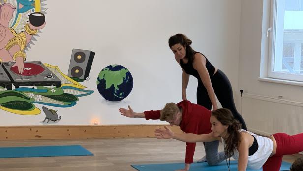 Die Yoga-Lehrerin unterstützt zwei Turnerin beim Muskeltraining auf der Matte.
