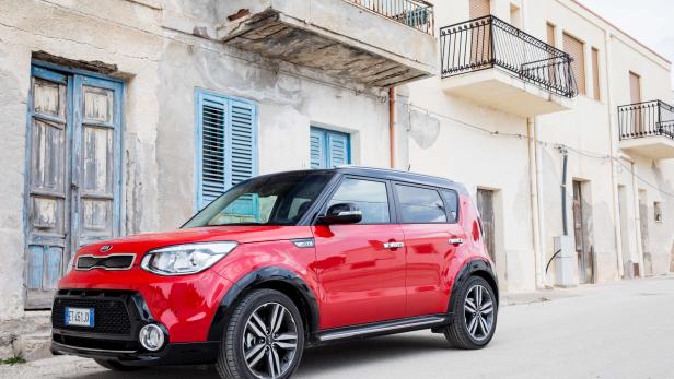 Ein roter Kia Soul parkt vor einem alten Gebäude mit blauen Fensterläden.