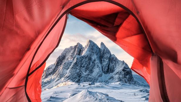 Blick aus einem roten Zelt auf eine verschneite Berglandschaft.