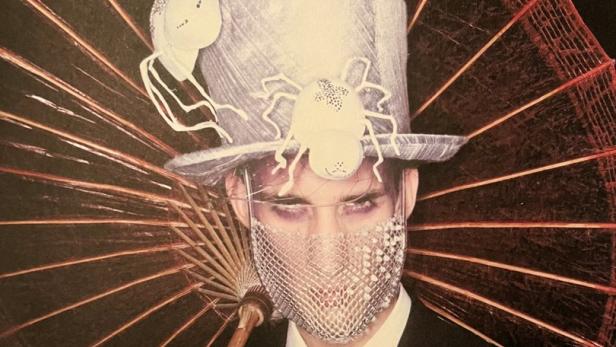 Ein Mann mit Zylinder, Spinnen und Maske hält einen Sonnenschirm.