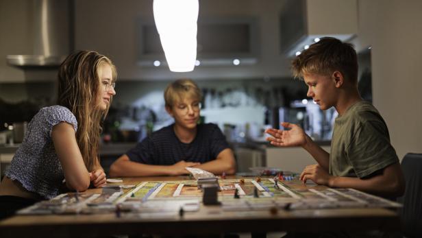 Drei Jugendliche sitzen an einem Tisch und spielen ein Brettspiel.
