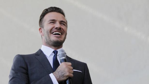 David Beckham lacht, während er ein Mikrofon hält.